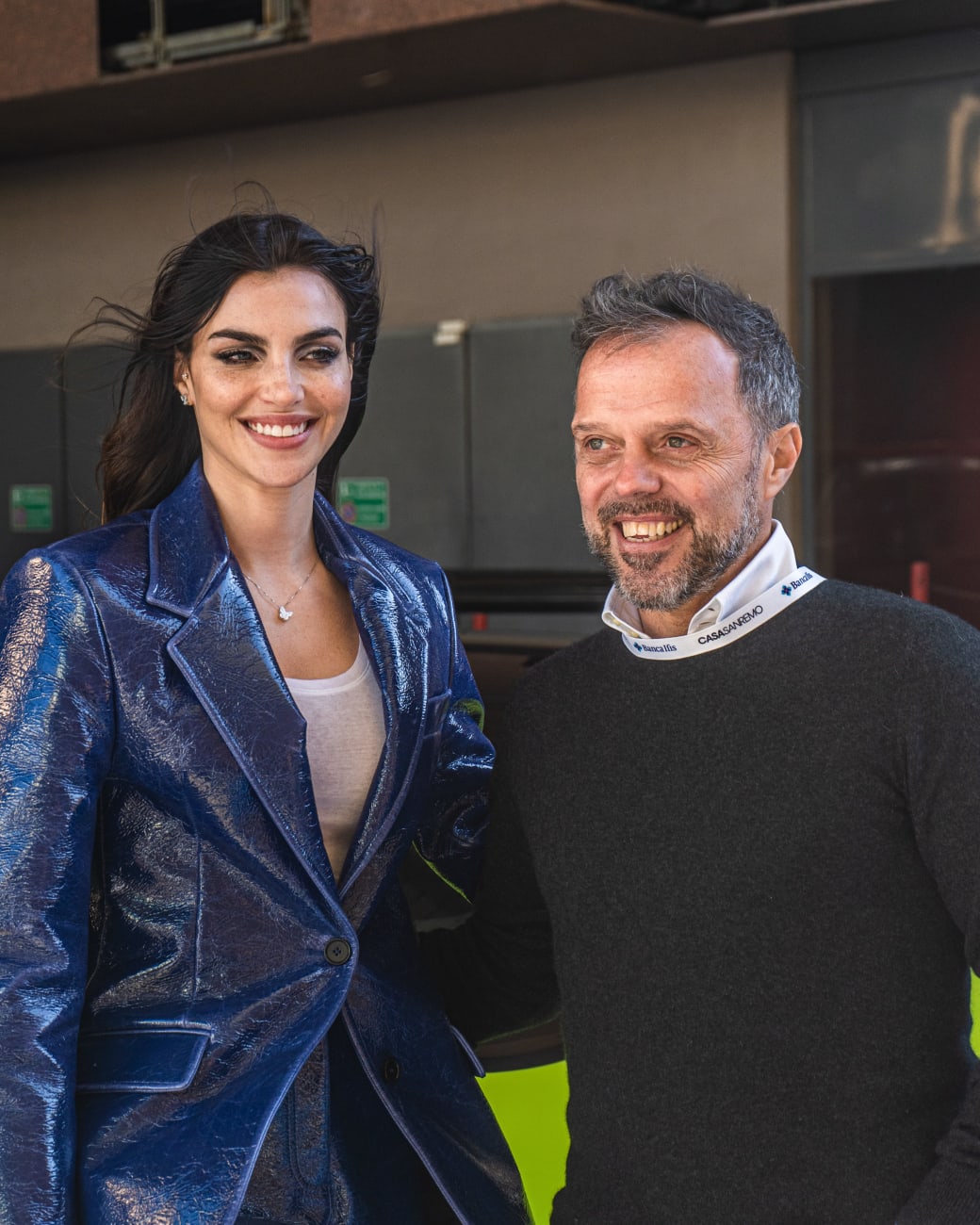 Due ospiti sorridenti all’arrivo a Casa Sanremo: giacca blu metallizzata e camicia con il colletto brandizzato Casa Sanremo Banca IFIS