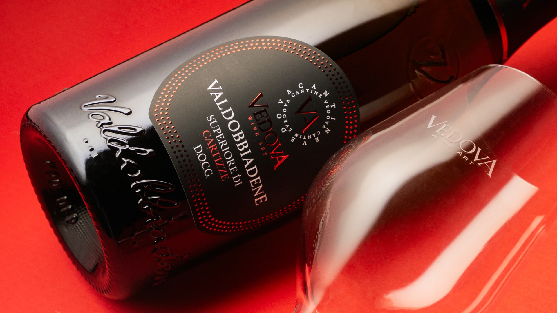 Bottiglia di vino Vedova con etichetta elegante, posizionata su un tavolo in legno con bicchiere di vino rosso accanto