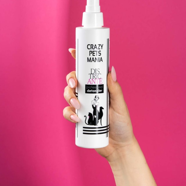 Mano che regge il flacone spray del districante Crazy Pets Mania su fondo fucsia