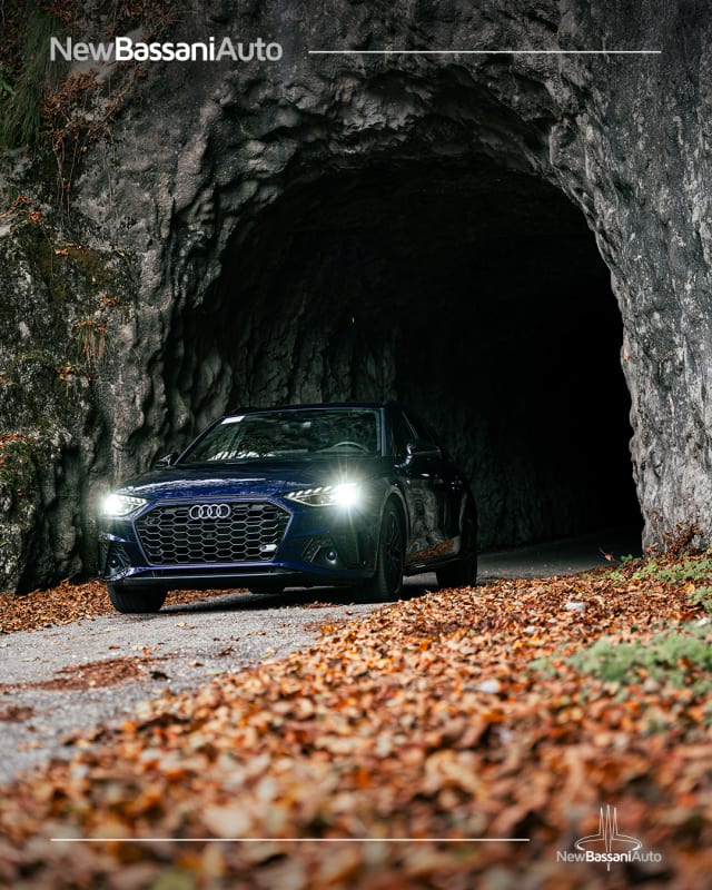 Audi A4 blu con i fari accesi all’uscita di una galleria nella roccia, tra le foglie d’autunno, in un post di New Bassani Auto