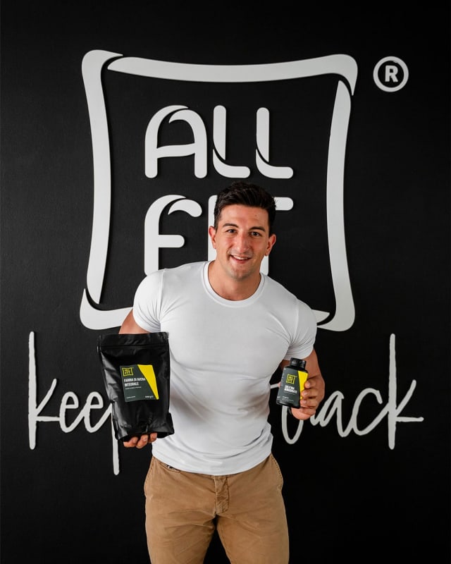 Ragazzo mostra la busta di farina di avena integrale e un barattolo di integratore All Fit davanti alla parete nera con il logo e il claim «keep on track»