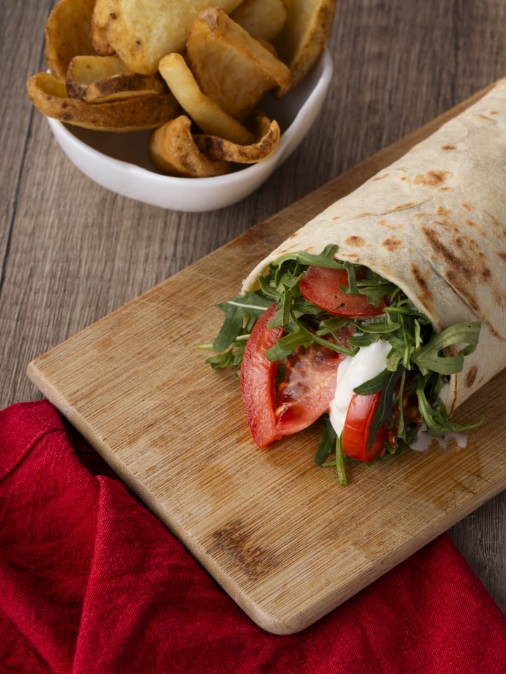 Piadina La Caveja con prosciutto, pomodoro e insalata su tagliere, con patate