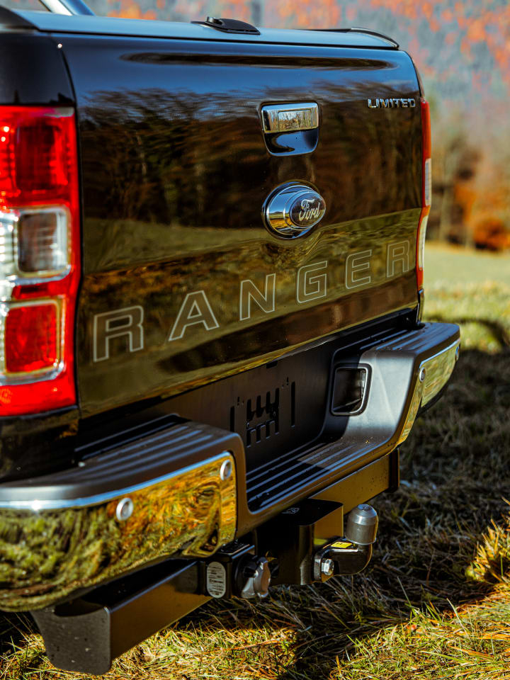 Portellone di un Ford Ranger Limited nero con la scritta RANGER e il gancio traino, parcheggiato su un prato d’autunno