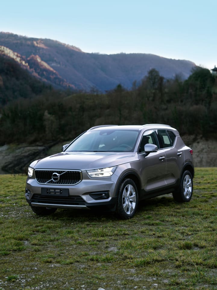 Volvo XC40 grigio su un prato, con i boschi e le montagne sullo sfondo