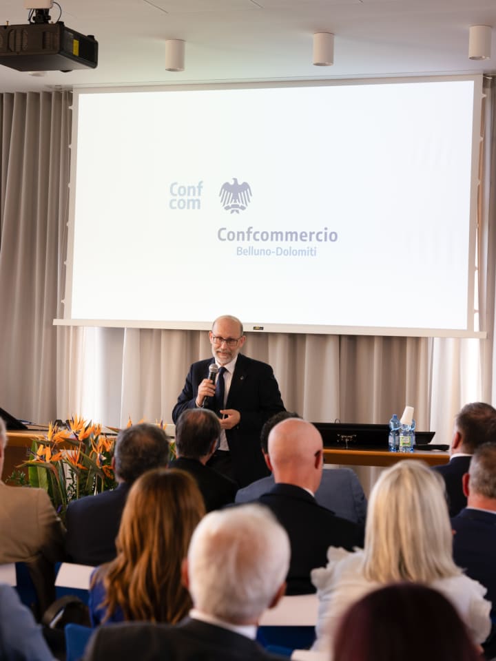 Intervento al microfono davanti al marchio Confcommercio proiettato in sala