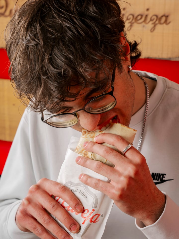 Ragazzo con occhiali che addenta una piadina La Caveja