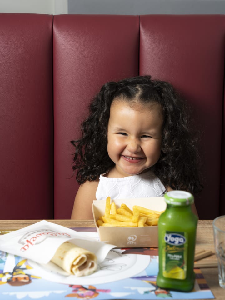 Bambina sorridente al tavolo con piadina e patatine La Caveja