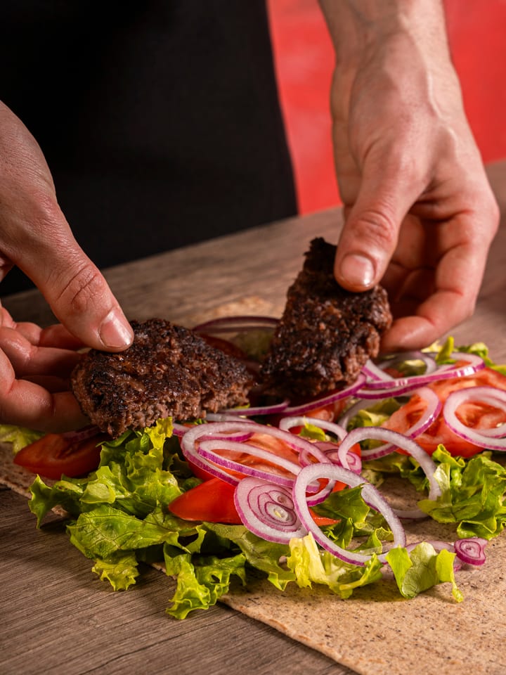 Mani che compongono una piadina aperta con affettati, rucola e cipolla