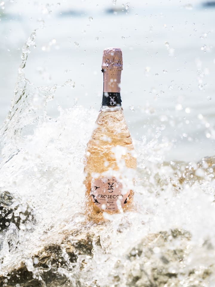Bottiglia di Prosecco Rosé tra gli spruzzi delle onde sugli scogli