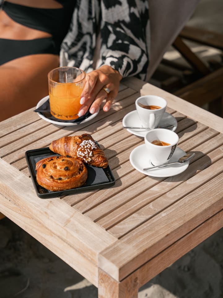 Colazione al tavolino in teak: spremuta d’arancia, due caffè espresso e un vassoio con croissant e girella all’uvetta