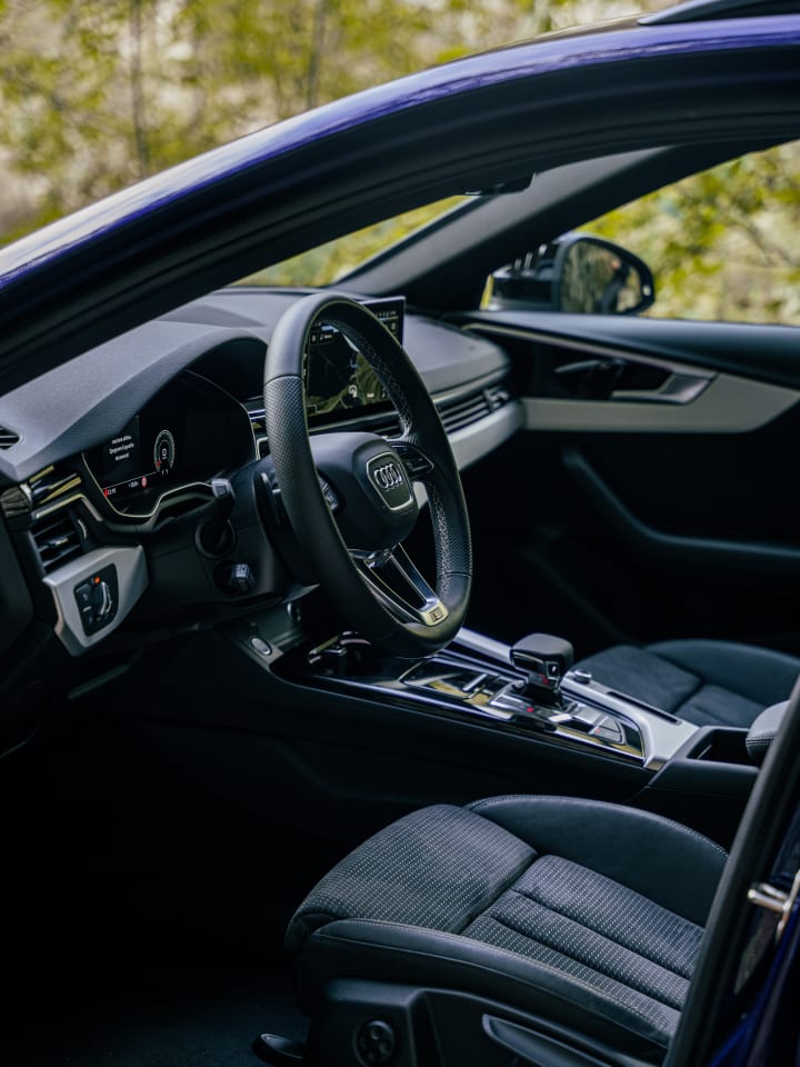 Posto guida di un’Audi blu con volante sportivo e quadro strumenti digitale, visto dalla portiera aperta