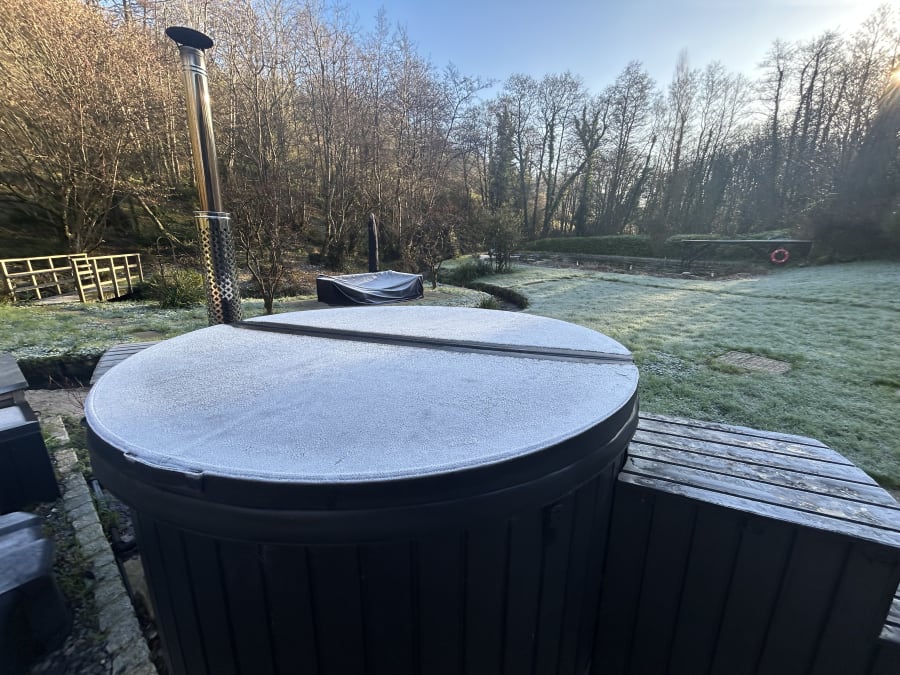 Guests soaking in the wood-fired hot tub at dusk at Hole Mill, Devon