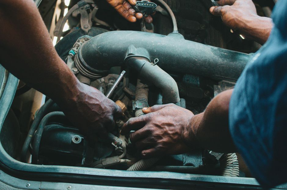 Close-up of mechanics working on a vehicle engine, showing teamwork and precision in car maintenance.