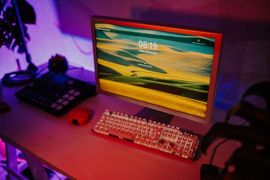 A sleek computer desk with colorful lighting, keyboard, monitor, and audio equipment creating a modern workspace.