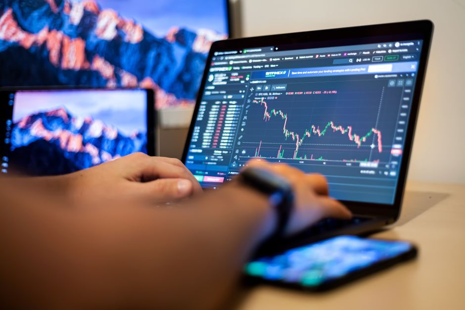 Hands typing on a laptop displaying financial trading charts, indicating active online trading work.