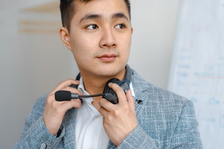 Close-up of an Asian adult man wearing a headset, depicting focus and professionalism indoors.