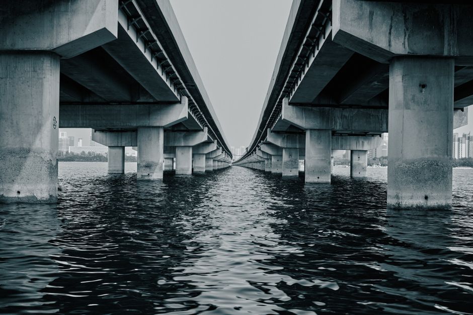 Black and white photograph of a symmetrical concrete bridge over a river in an urban setting.