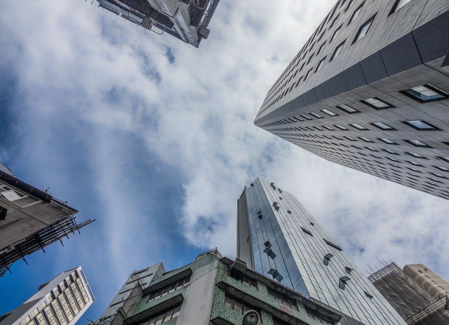 Dramatic perspective of city skyscrapers reaching towards a cloudy blue sky.
