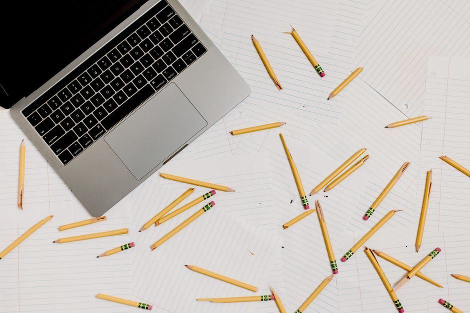 Top view of a workspace with a laptop, scattered pencils, and lined paper, ideal for educational themes.