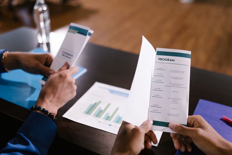 Hands examine program guide in a corporate meeting setting, highlighting agenda details.
