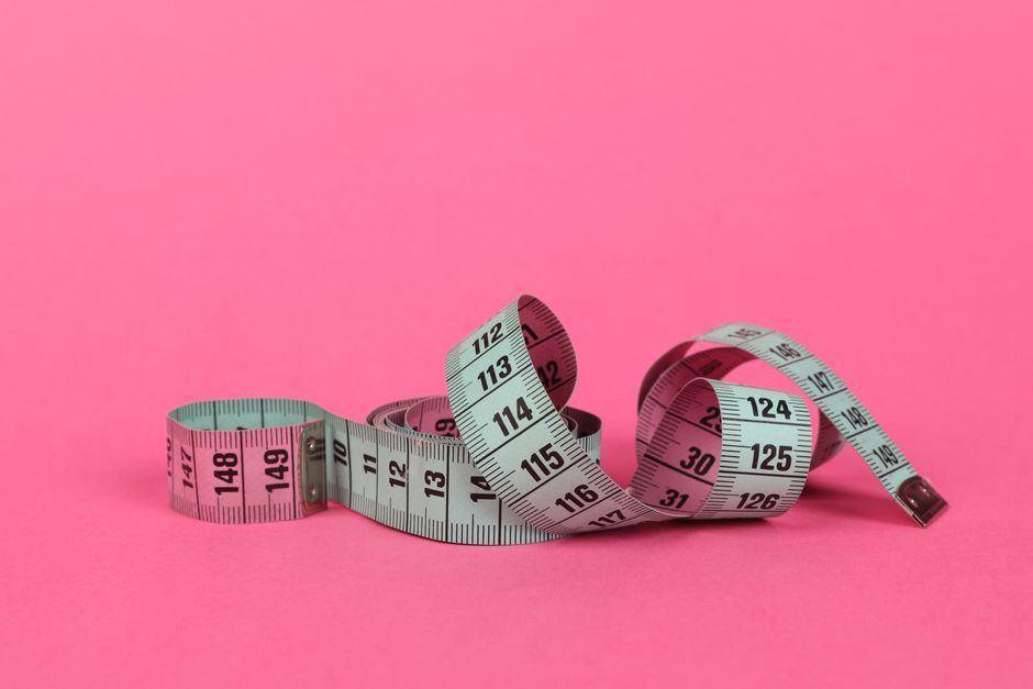 Close-up of a measuring tape on a vibrant pink background for design use.
