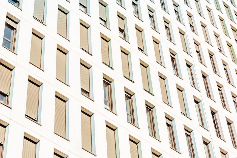 Exterior of tall multi storey modern building with lots of long narrow rectangular identical windows in sunlight