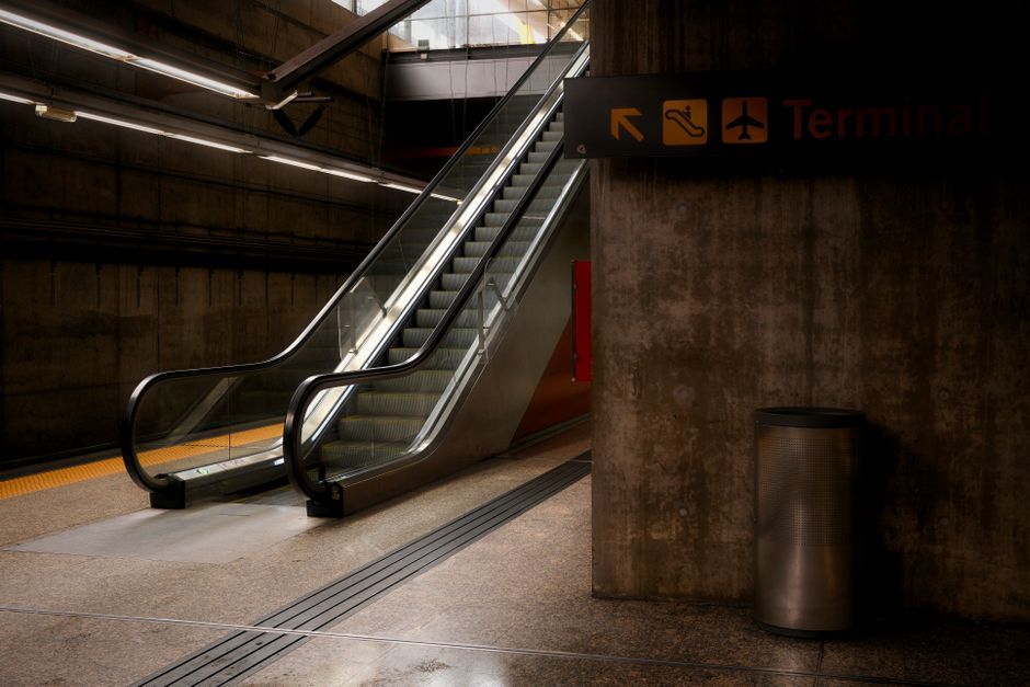 An empty airport terminal with an escalator leading to a terminal. Low light setting.