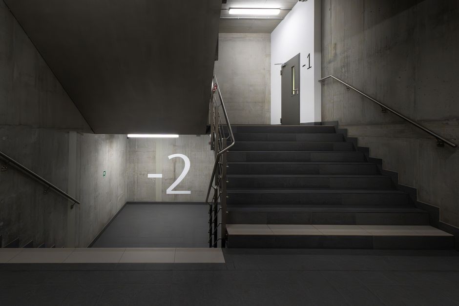 A minimalist underground stairwell with concrete walls and clear signage.