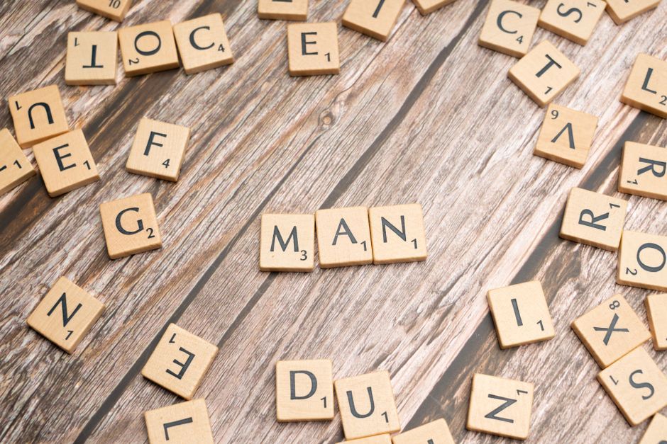 Wooden letter tiles arranged to spell 'MAN' on a rustic wooden surface.