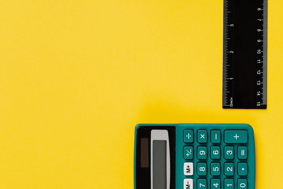 A bright teal calculator and black ruler on a vivid yellow surface. Ideal for educational themes.
