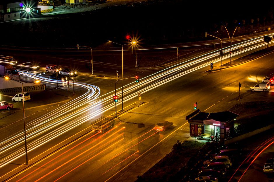 Aerial view of a city intersection at night, featuring vibrant light trails from passing vehicles.
