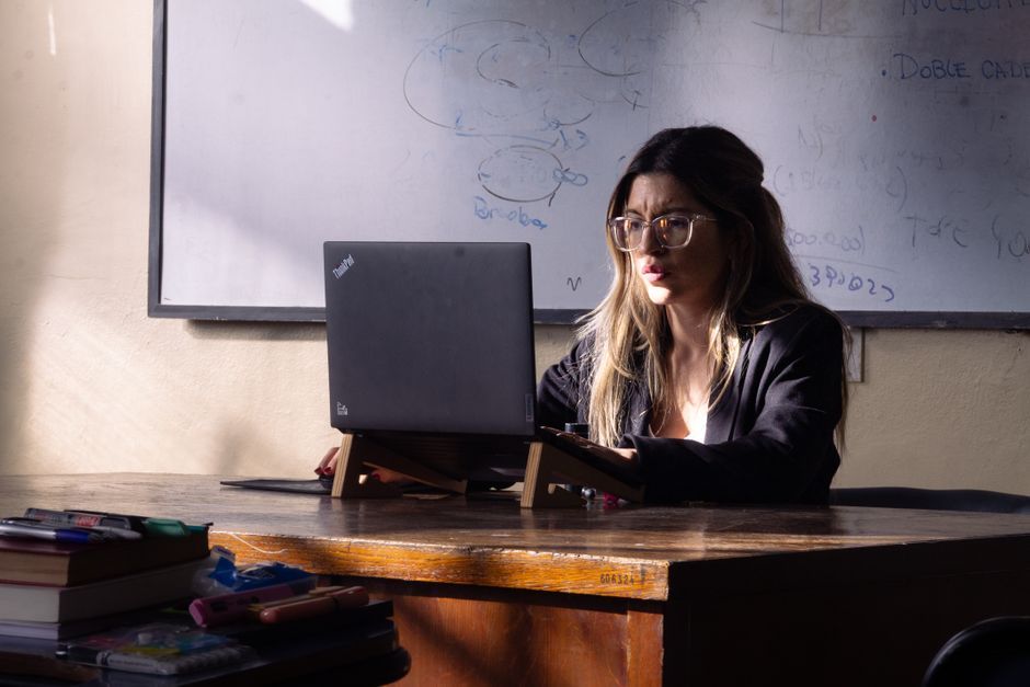A woman educator focuses on her laptop in a sunlit Buenos Aires classroom, promoting learning and concentration.