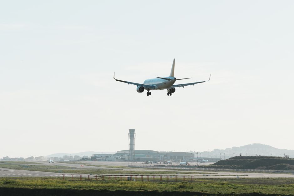 Modern airplane approaching runway for landing at a busy airport.