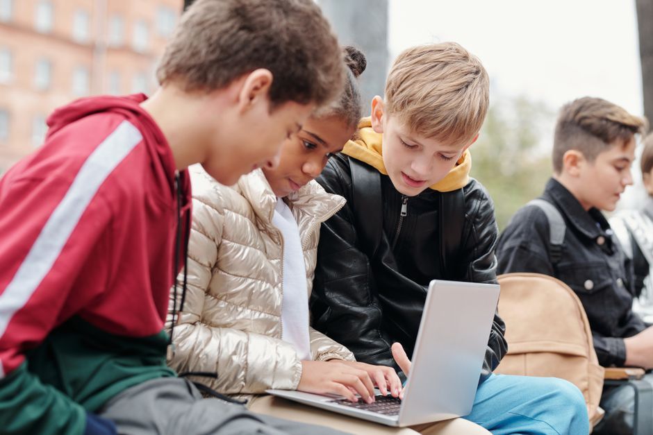Group of teenagers studying together on a laptop outdoors, fostering collaboration.