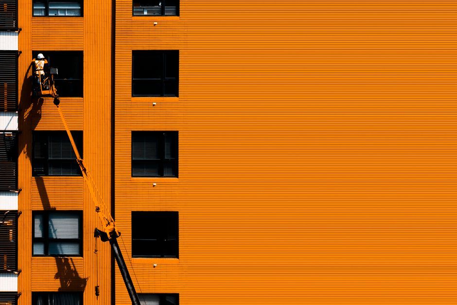 A construction worker using a cherry picker working on an orange building facade.