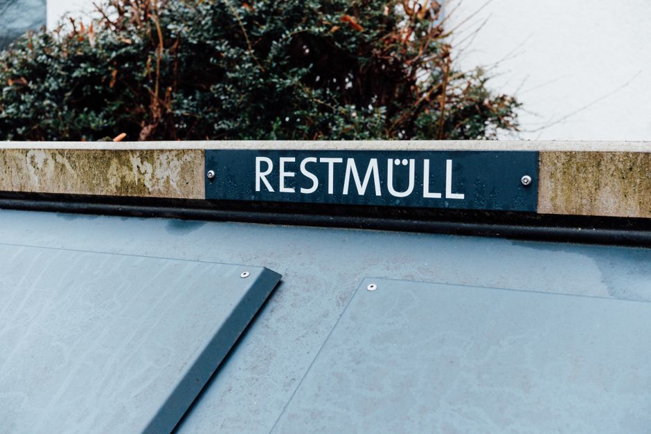 Photo of a Restmüll bin with a sign, against a backdrop of urban greenery.
