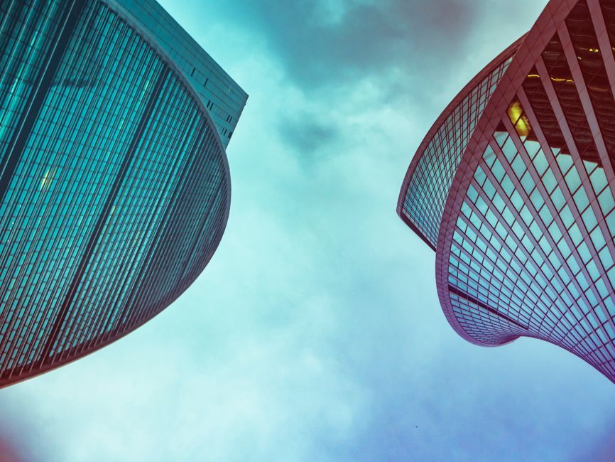 Low angle view of modern glass skyscrapers with curved designs under a cloudy sky.