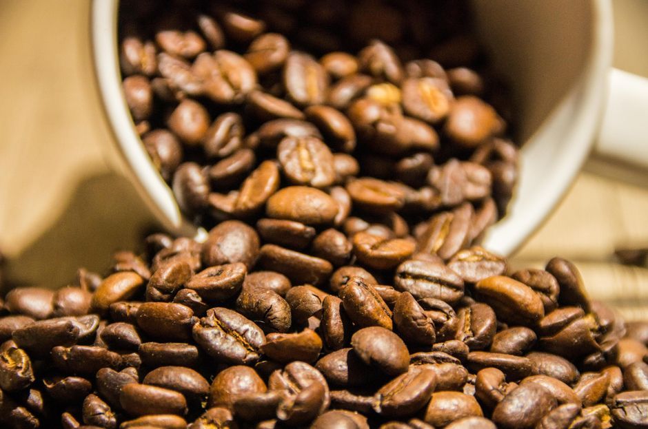 Rich, aromatic roasted coffee beans spilling from a white mug. Perfect for coffee lovers.
