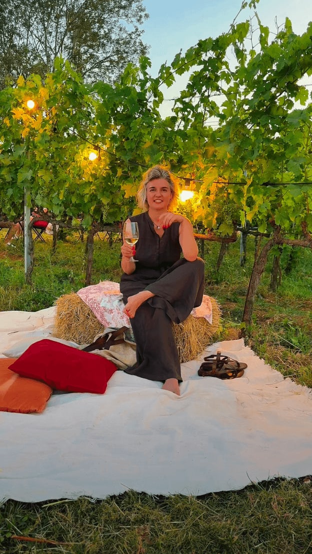 Donna seduta in vigneto al tramonto con calice di vino. Content creation lifestyle per branding e social media.