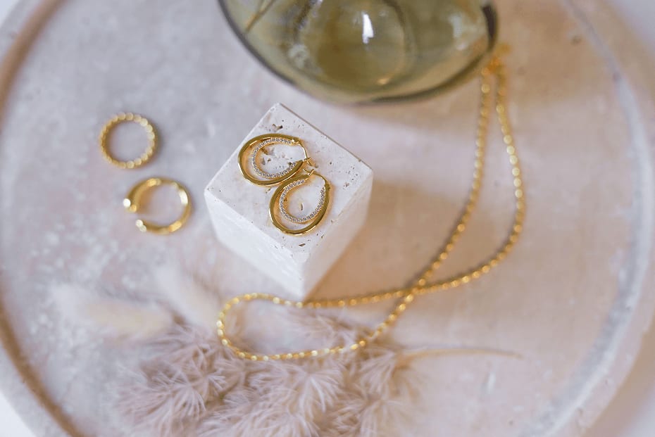 Art direction e creazione contenuti visivi per brand di gioielli Numi: set design con orecchini a cerchio e cristalli su pietra naturale, circondati da texture soft e toni beige.