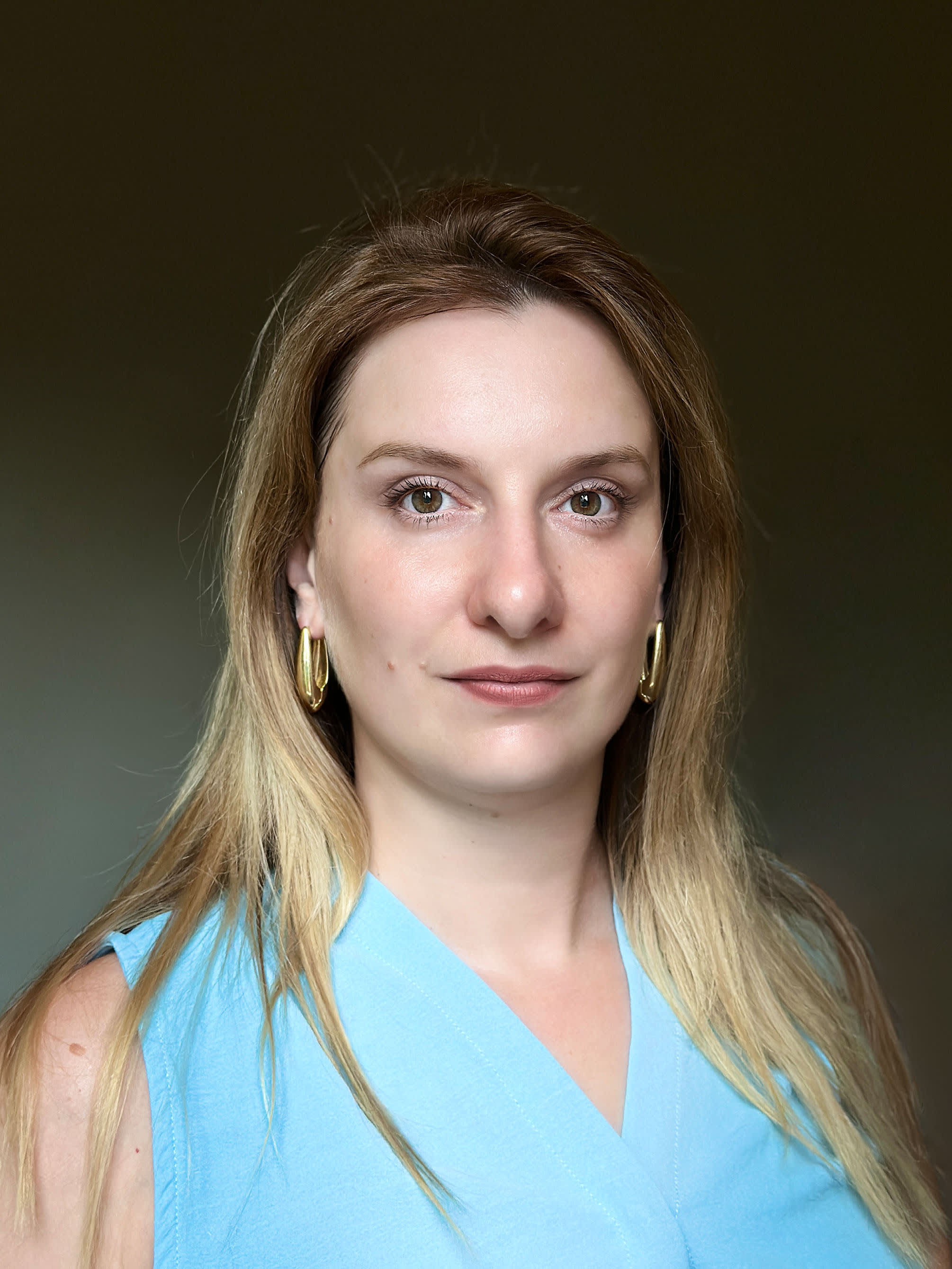 Ritratto professionale di Valentina Fetisova, digital strategist e brand consultant, con top azzurro e orecchini dorati su sfondo neutro.