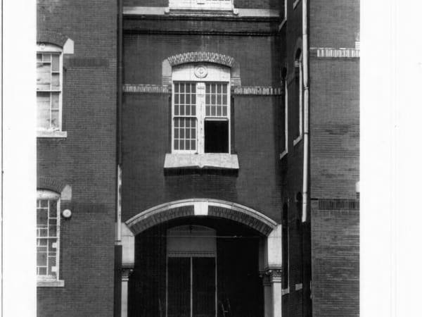 Detail of the south entrance, east elevation, facing west: segmental stone arch with alternating brown and black glazed brick above square columns.