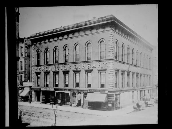 Mercantile Library Hall: Mercantile Library Hall at Fifth and Locust before 1887, with shops on the ground floor and the Grand Hall's arched windows above.