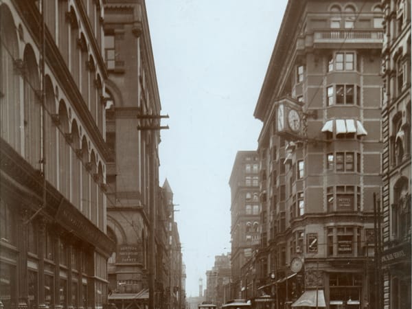 Mercantile Library Building: Looking west on Locust from Broadway: the 1889 Mercantile Library Building's arcaded Romanesque front on the left, the Mermod-Jaccard Building and its clock on the right. Photograph by Emil Boehl.