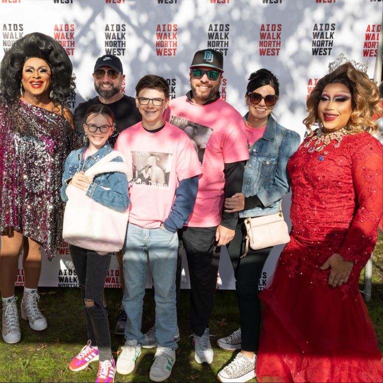 people posing with drag queens in front of Aids Walk banner