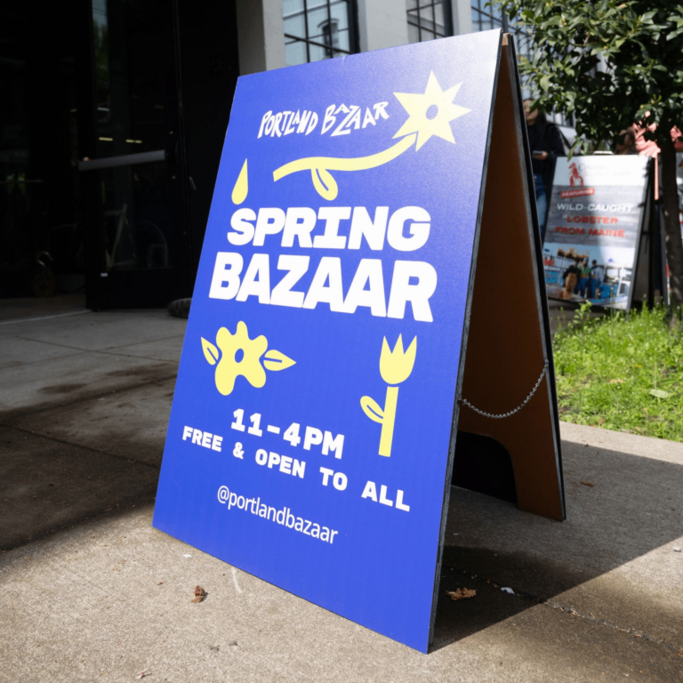 a sandwich board with name of Spring Bazaar with dates and times it is open