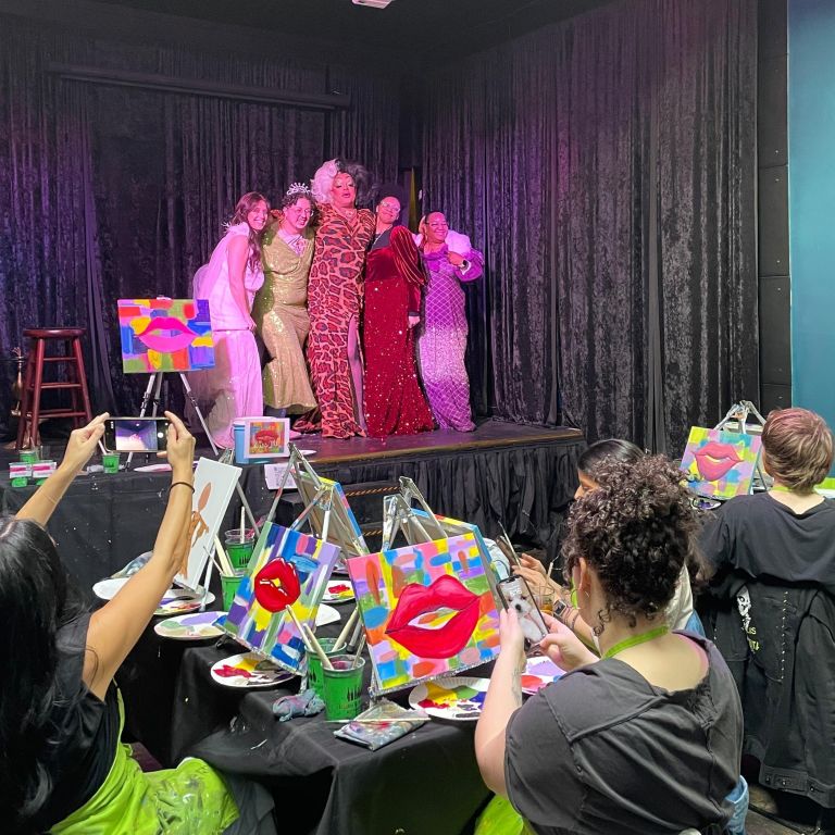 a drag queen on stage with people painting at tables watching