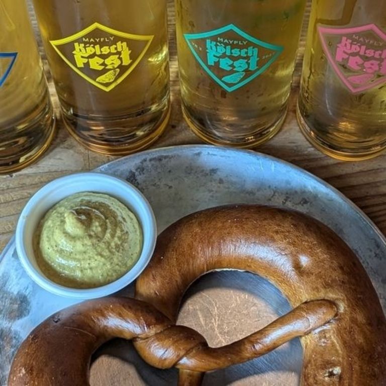 glasses of beer lined up next to a pretzel and mustard on a plate
