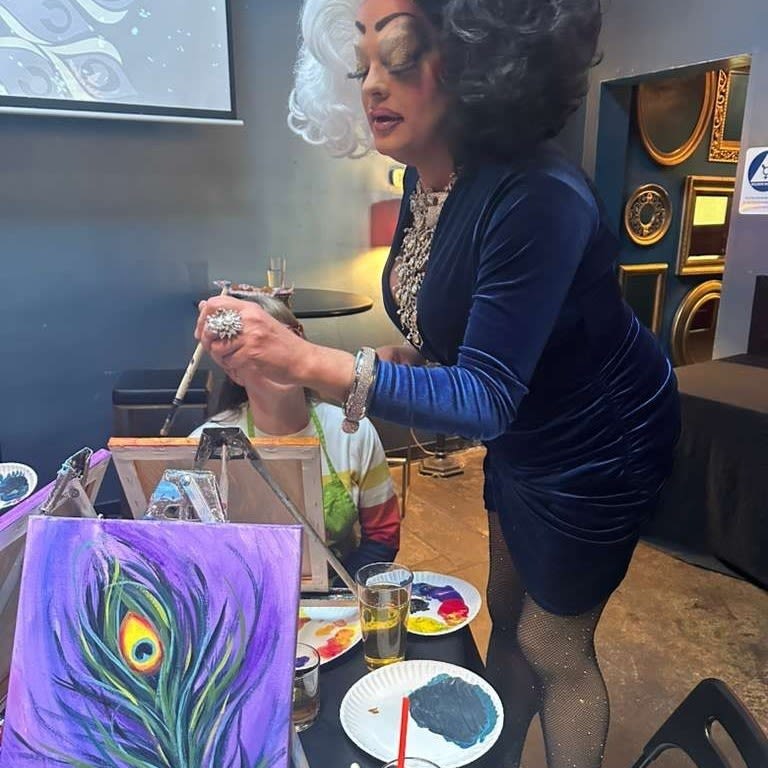 a drag queen assisting people painting