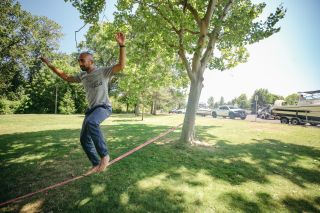 A man balances on a slack line connected to a tree in a park